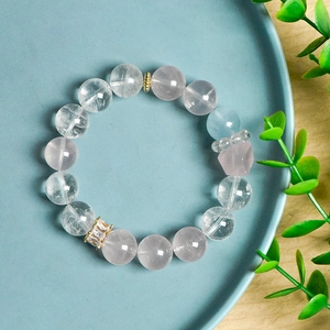 Natural pink crystal 12mm bead bracelet with aquamarine and gold accents on a blue plate