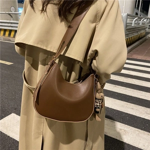Brown crescent hobo bag with teddy charm on beige trench coat in night street view