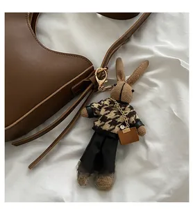 Detail of knitted rabbit charm with houndstooth sweater on a brown leather saddle bag