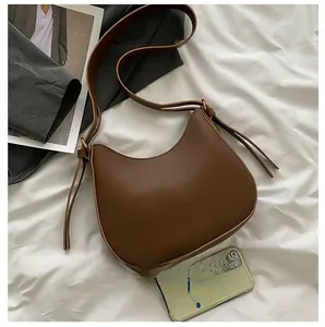 Brown matte saddle bag with long tassels and adjustable strap shown on white sheets
