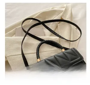 Detail of black quilted shoulder bag with gold clasp and woven handle on beige blazer