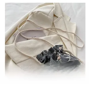 Detail of grey fabric bucket bag featuring pink floral embroidery and rope strap