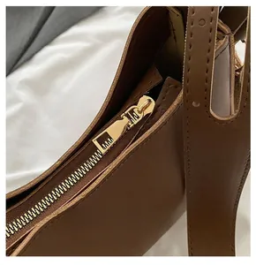 Detailed macro view of the smooth gold metal zipper and stitching on the brown saddle bag