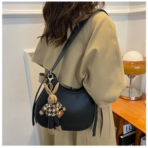 Black saddle bag with brown houndstooth rabbit charm worn on the shoulder by a model