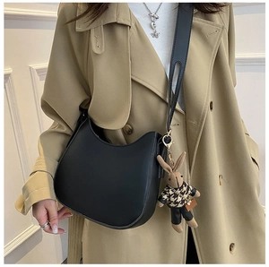 Detail of a black half-moon saddle bag with a cute plush rabbit charm on a trench coat