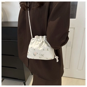 Detail of cream fabric drawstring bag with floral embroidery and crossbody strap