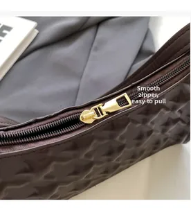 Close-up of the smooth golden zipper and quilted diamond texture on dark brown handbag