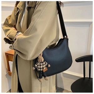 Detail of a black matte hobo bag with a cute rabbit pendant on a beige trench coat