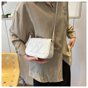 Detailed shot of a white quilted crossbody bag with gold chain strap on a model