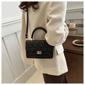 Detail of black triangular quilted crossbody bag with golden twist lock and top handle