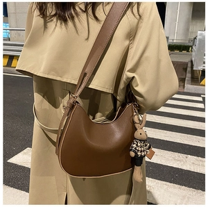 Brown leather crescent hobo bag with a cute rabbit pendant shown on a beige trench coat