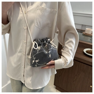 Detail of grey canvas crossbody bag with white floral embroidery and drawstring closure