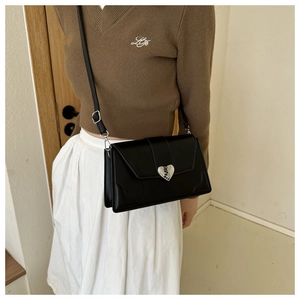 Detail of a black square leather crossbody bag with a silver heart-shaped lock buckle
