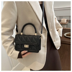 Detail of black quilted crossbody bag with gold twist lock on an ivory suit background