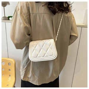 Model wearing a white quilted crossbody bag with an elegant woven metal chain strap