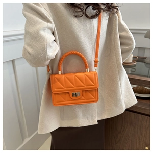Detail of orange quilted crossbody bag with metal twist lock and woven top handle strap