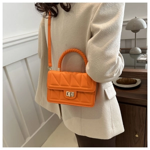 Detail of orange quilted crossbody bag featuring V-stitch pattern and gold turn-lock closure