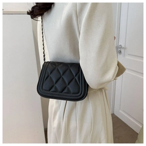 Detail of a black quilted crossbody bag with gold-tone chain strap on a model