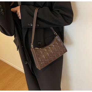 Detail of dark brown baguette bag with quilted texture and gold zipper on a model shoulder