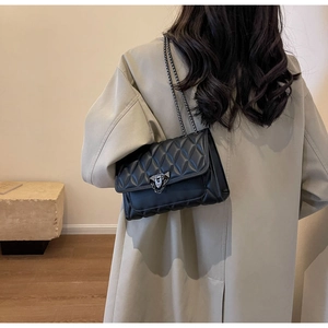 Close-up of black quilted crossbody bag with silver V-clasp on a beige coat