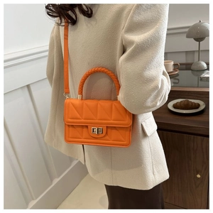 Detail of orange quilted crossbody bag with woven handle and metallic turn-lock closure