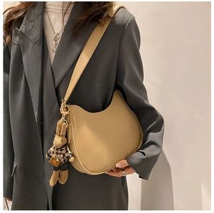 Detail of hobo saddle bag in beige leather with cute rabbit doll pendant on grey suit