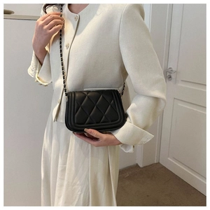 Close-up of black quilted leather crossbody bag with gold chain strap on white dress