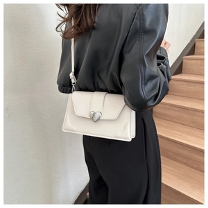 Detail of a creamy white leather crossbody bag featuring a silver heart lock and stitching