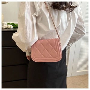 Detail view of pink quilted crossbody bag with metal chain strap on model's shoulder