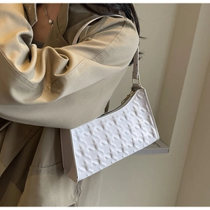 Detail view of cream baguette bag with geometric woven texture and gold zipper closure