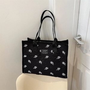 Sac fourre-tout en toile noire à imprimé rose blanche posé sur une chaise minimaliste