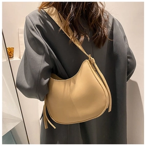 Beige crescent saddle bag with smooth faux leather finish and knot detail worn on shoulder