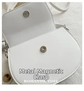 Detailed close-up of the silver magnetic buckle on a white leather saddle bag
