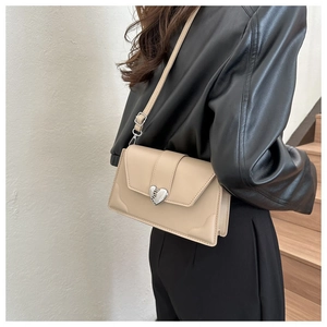 Detail of beige square crossbody bag featuring a silver heart-shaped lock and wavy stitching