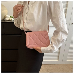 Close-up of light pink quilted crossbody bag with gold chain strap on a model