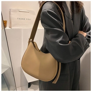 Close-up of a minimalist beige saddle bag worn by a model in a grey blazer suit