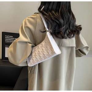 Detail of white underarm bag with embossed star pattern worn by a model in a trench coat