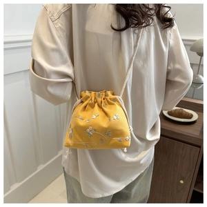 Detail of yellow canvas drawstring bag with delicate floral embroidery and braided strap