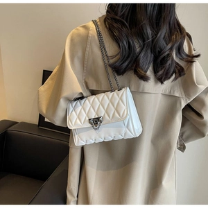 Detailed view of white quilted crossbody bag featuring silver metallic lock and chain strap