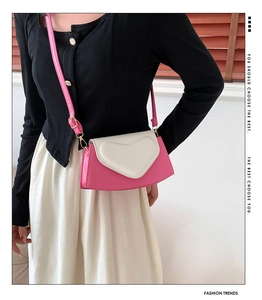 Detail of a pink and white crossbody bag featuring a unique heart-shaped flap and leather strap