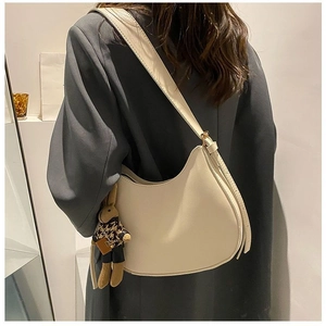 Detail of a minimalist off-white saddle bag with a cute rabbit pendant on a grey blazer
