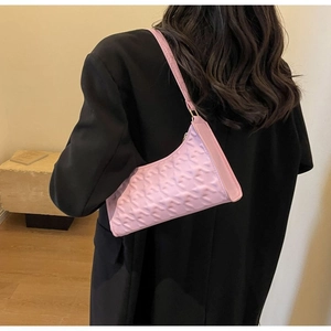 Detail of light pink shoulder bag with quilted texture shown on a model's shoulder