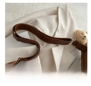 Detail of wide leather shoulder strap with neat stitching and a cute plush bear charm