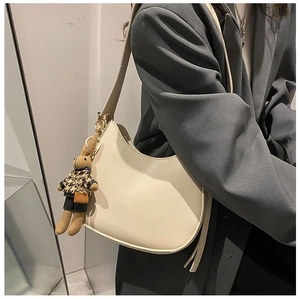 Close-up of cream crescent saddle bag with cute rabbit plush charm and wide strap
