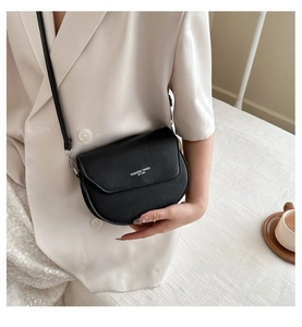 Detail of a matte black saddle bag featuring fashion trend lettering and a slim shoulder strap