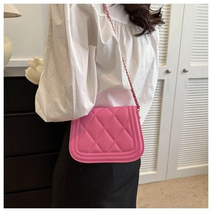 Detail view of pink quilted crossbody bag with metal chain strap worn by a model