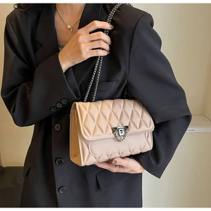 Close-up of beige quilted crossbody bag with silver metal lock and chain strap detail