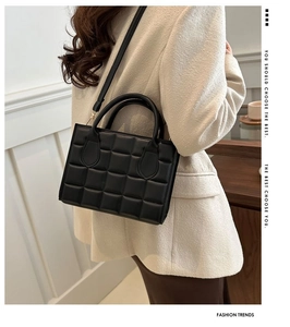 Detail view of black quilted leather handbag with structured handles and adjustable strap