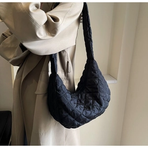 Detail of black quilted nylon crescent bag worn over a trench coat on a model