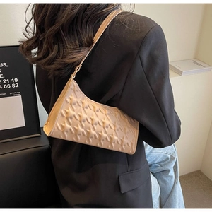 Detail of light beige underarm bag with embossed star pattern worn with a black blazer